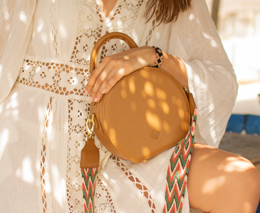 Close up photo of a woman holding a sandy coloured handbag with a Catalina strap attached