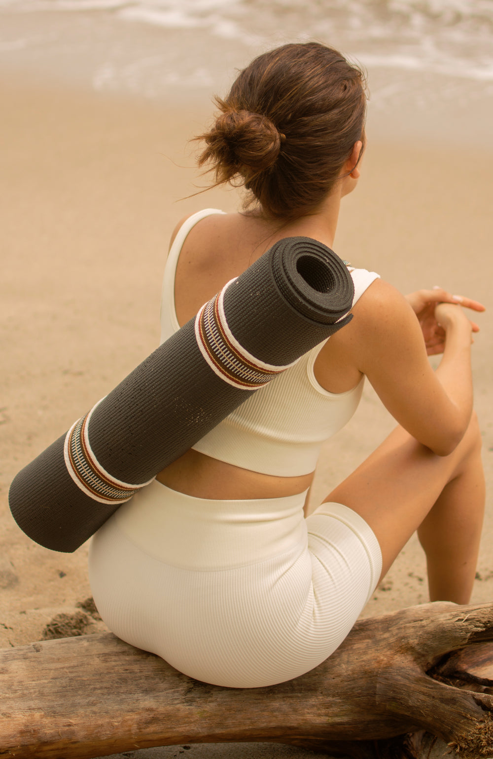 Woman sat on the beach wearing a yoga mat and strap on her back