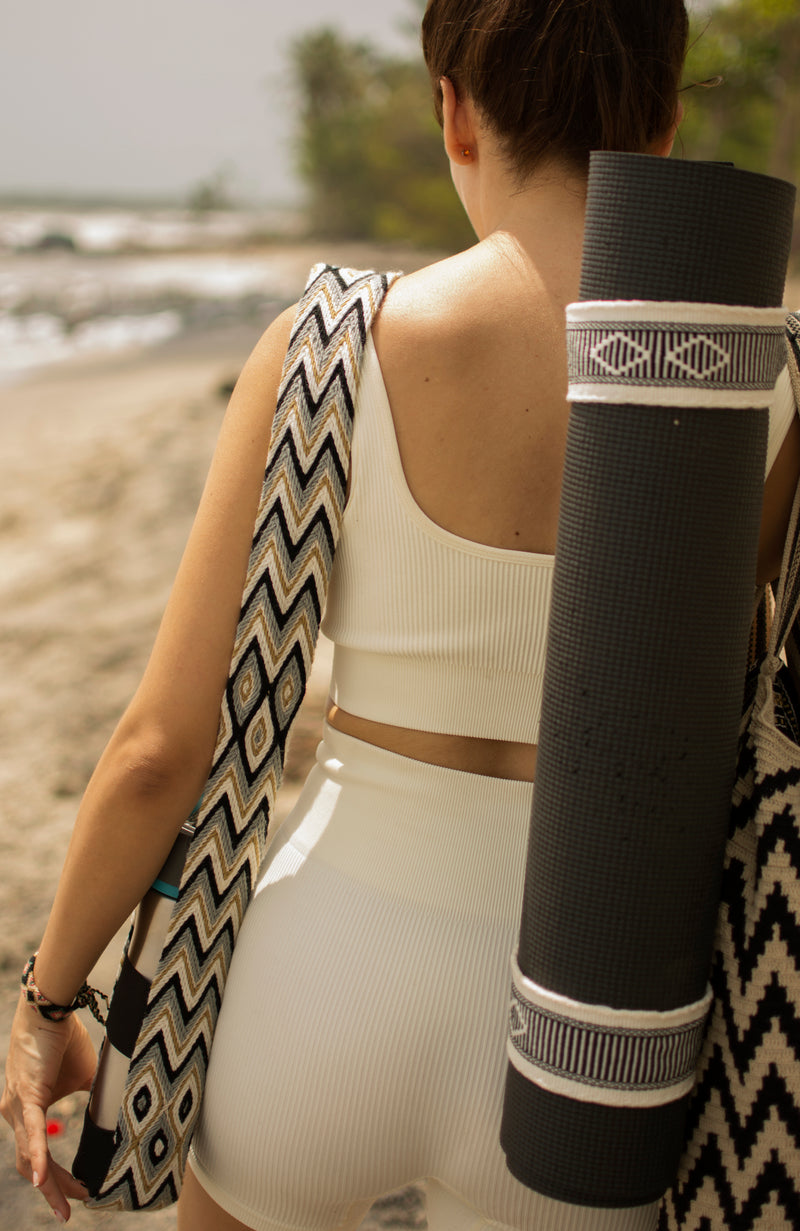 Close up of a woman in white carrying a yoga mat and water bottle over her shoulders, both with matching Catalina straps