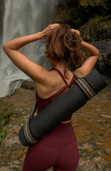 Woman stood in front of a waterfall carrying a yoga mat on her back, with a Catalina strap attached