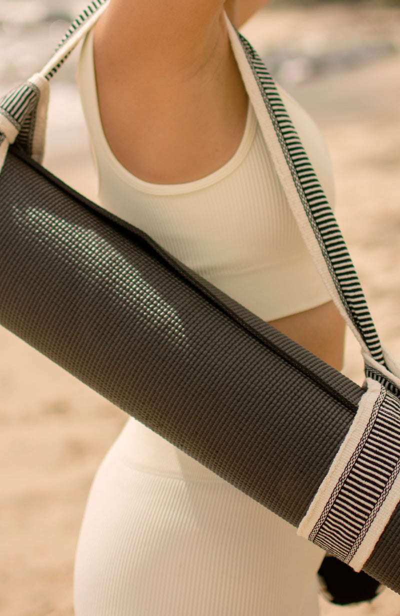 Close up of a woman in white carrying a yoga mat and Catalina strap over her shoulder